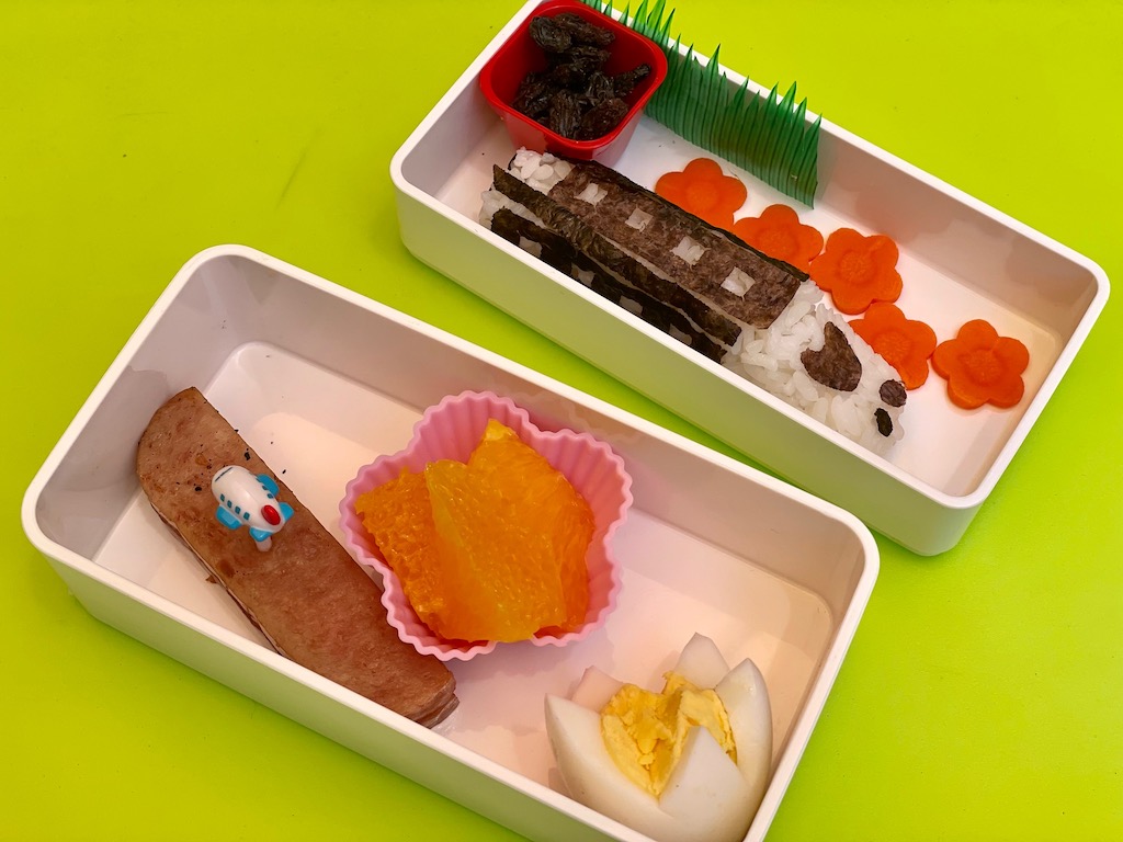 Little N made this bento: spam, orange segments, egg flower, bullet train onigiri, carrot flowers, and dried cranberries.