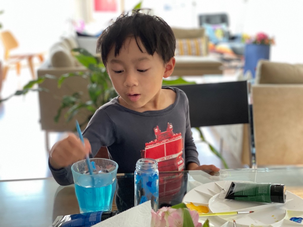 Child paints discarded spice bottles with acrylic paints.
