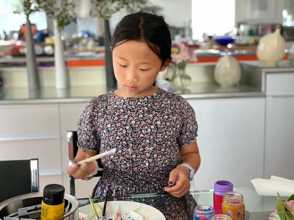 Child paints discarded spice bottles with acrylic paints.