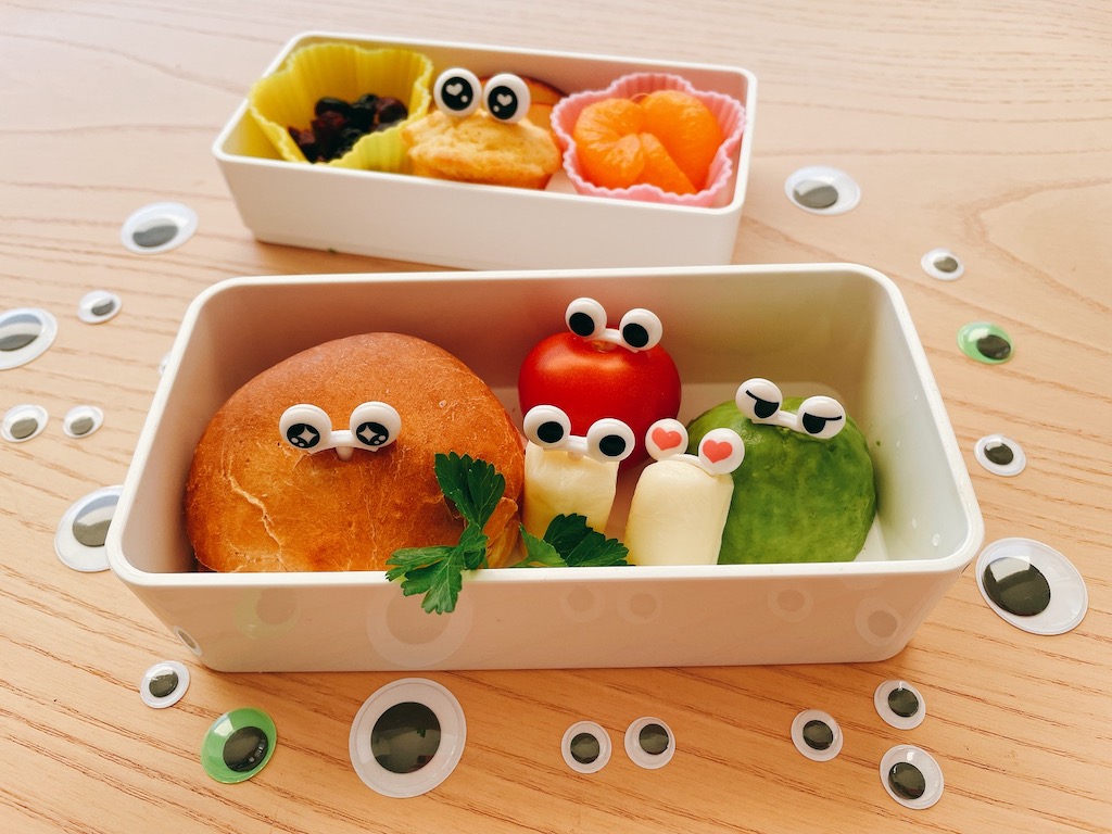 This bento gets its cuteness from eye picks that peek out of a sandwich, cherry tomato, string cheese, avocado ball, and mini cornbread.
