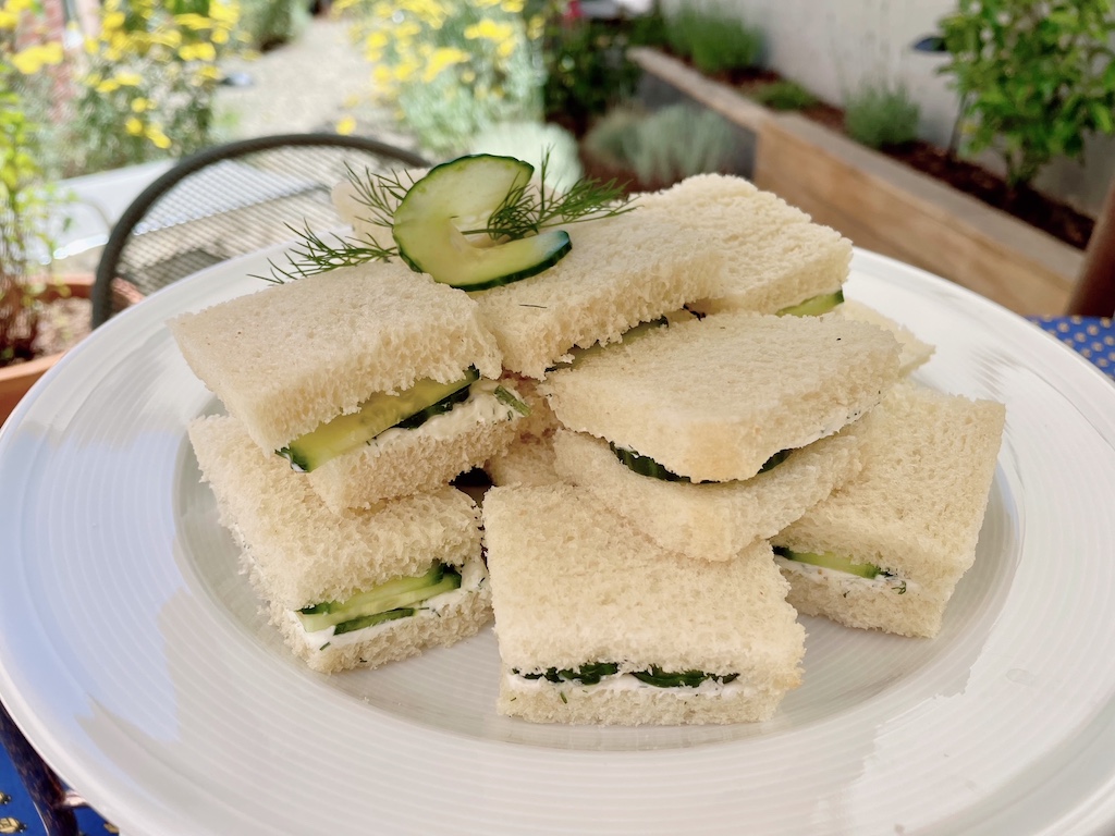 Cucumber tea sandwiches are stacked and the whole garnished with a cucumber slice and sprig of dill.