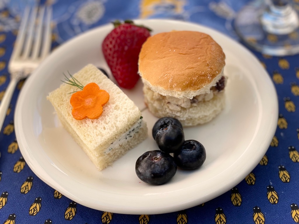 A sampling of simple party food: cucumber tea sandwich garnished with a carrot flower and sprig of dill, curried chicken sandwich on Hawaiian roll, and a few berries. 