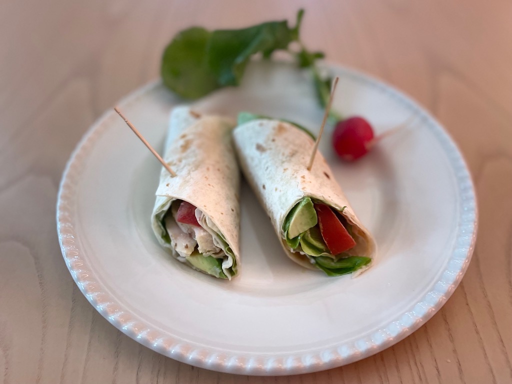 This turkey sandwich uses a flour tortilla to wrap around turkey slices, butter lettuce, avocado, and tomato.