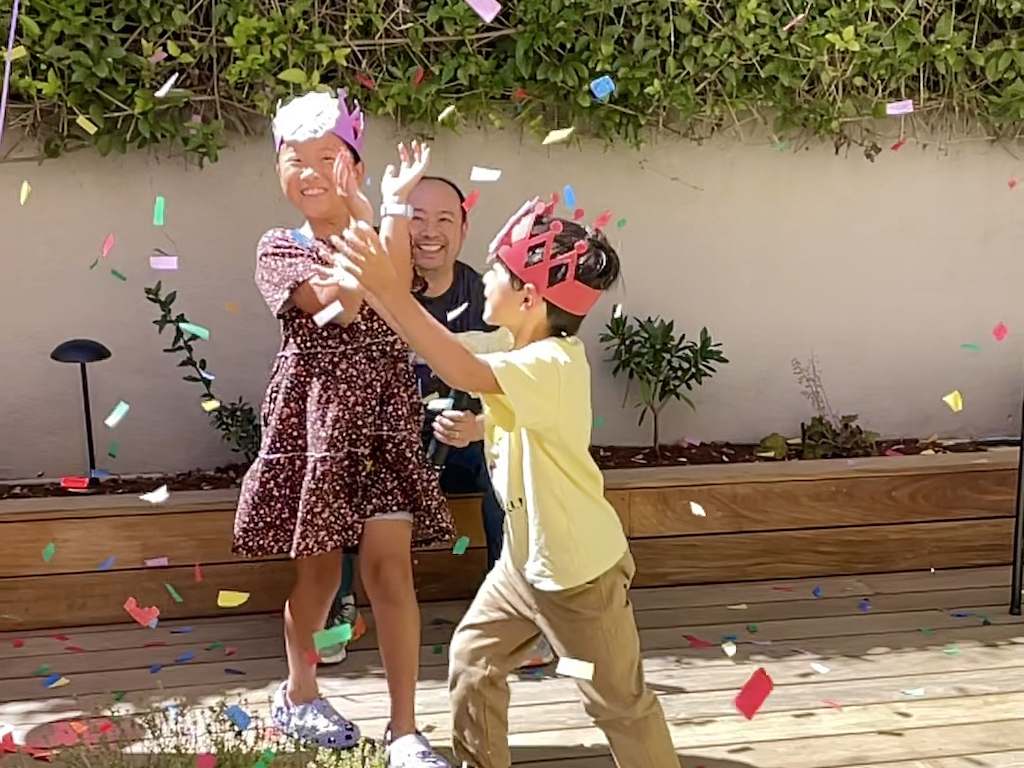 Kids capture tissue paper confetti from a confetti canon during a summer party.