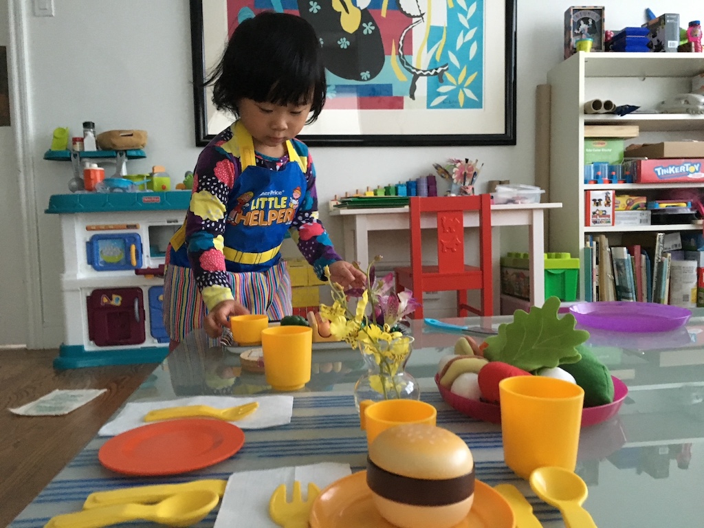 Child setting the table after "cooking" a meal on her kitchen set.