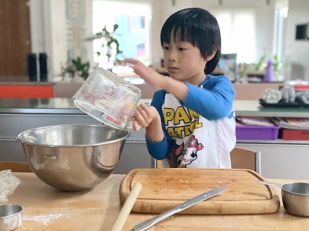 Child puts 4 cups of apple cubes into mixing bowl to toss with other ingredients.