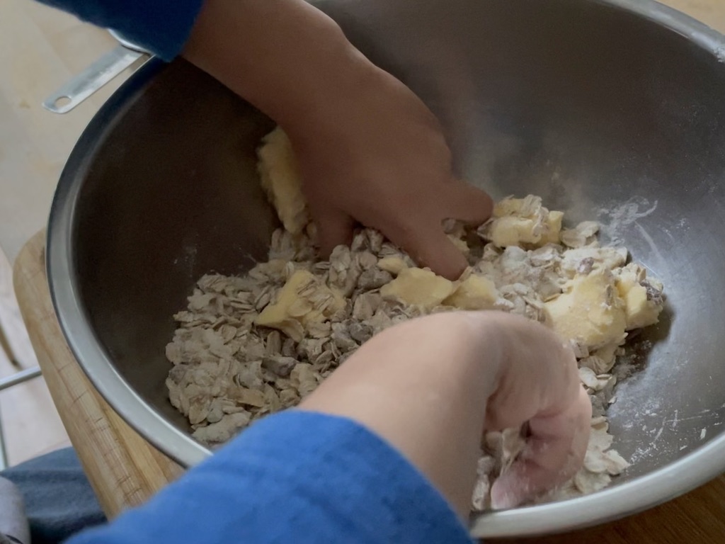Child uses hands to mix butter into dry ingredients for the topping.