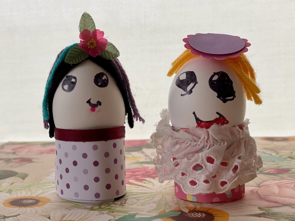 One egg doll has a flower in her hair. The other is wearing eyelet lace for a skirt.
