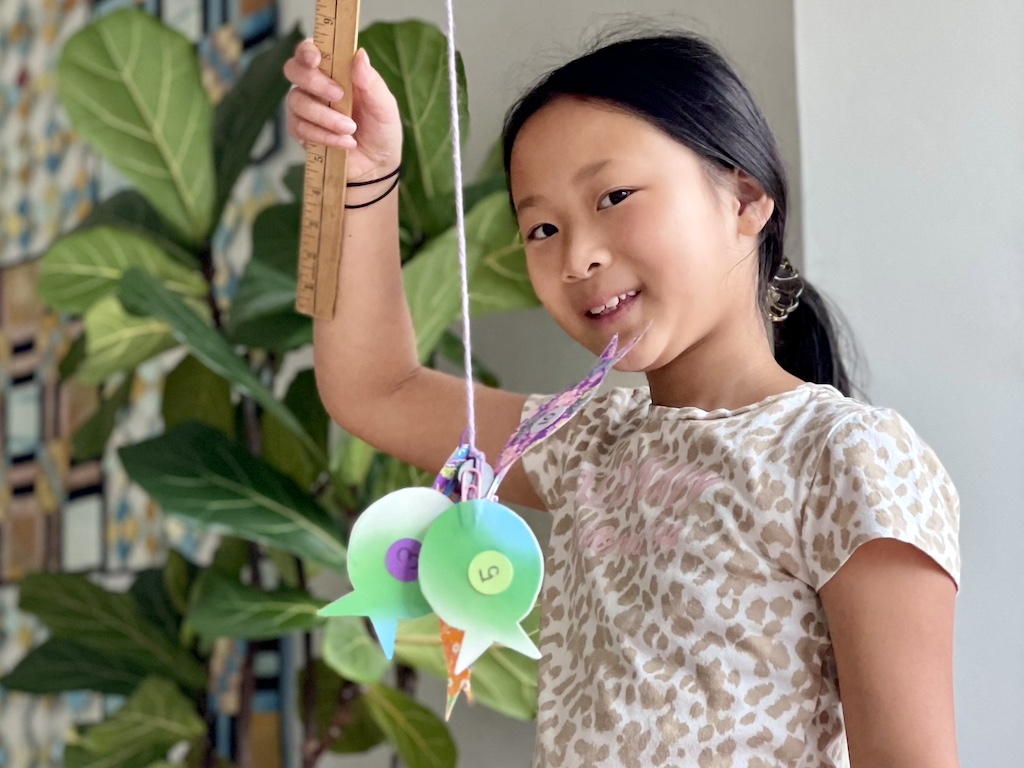 Child displaying catch of paper fish, during indoor play.
