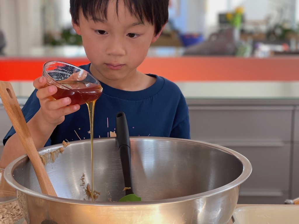 Child adds honey to make No-Bake Peanut Butter Cereal Bars--a tasty snack to develop healthy eating habits.