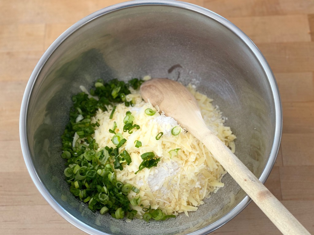 To make easy Irish soda bread with cheese and green onions, start by combining dry ingredients with the cheese and onions.