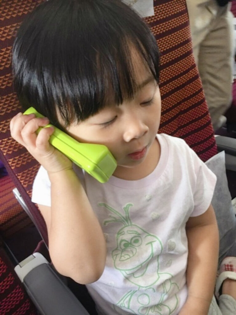 A child takes her green telephone on vacation to keep in touch with grandma from the airplane.