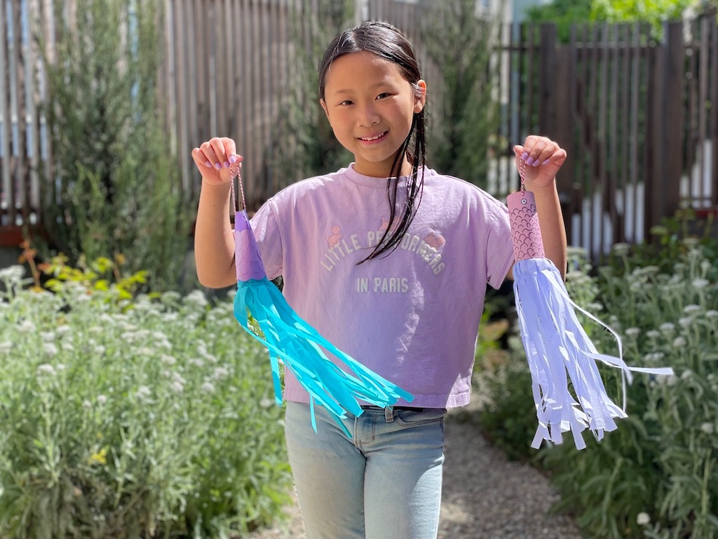 Child in the garden displays two koinobori carp she made from toilet paper rolls for Children's Day.