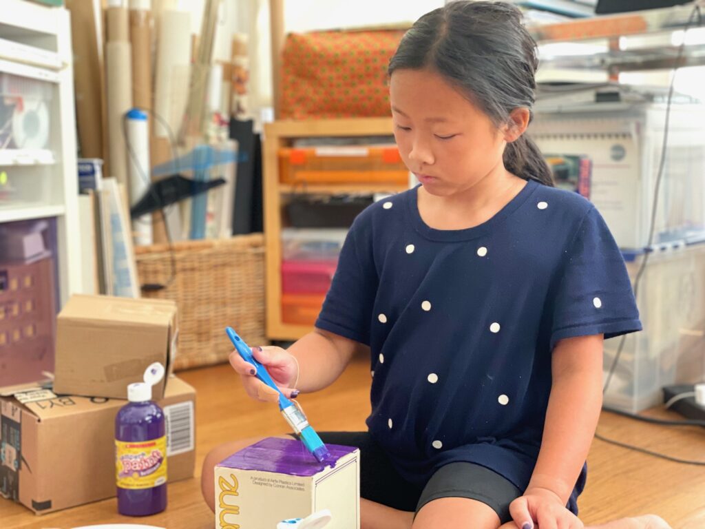 Child painting a cardboard box to make a house.