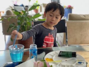 Child paints a discarded spice jar to make a vase.