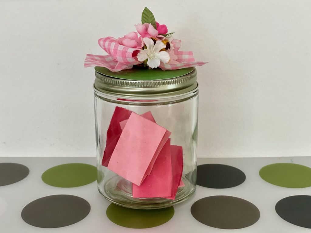 A Mother's Day Gift: Jar decorated with ribbons and flowers with paper slips inside containing messages of love and promises of services. 