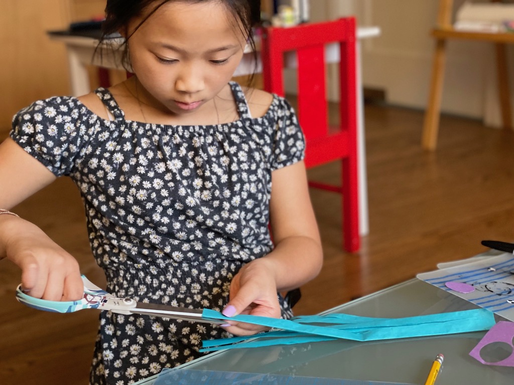 A child cuts tissue paper into strips to form the tail of the koinobori.