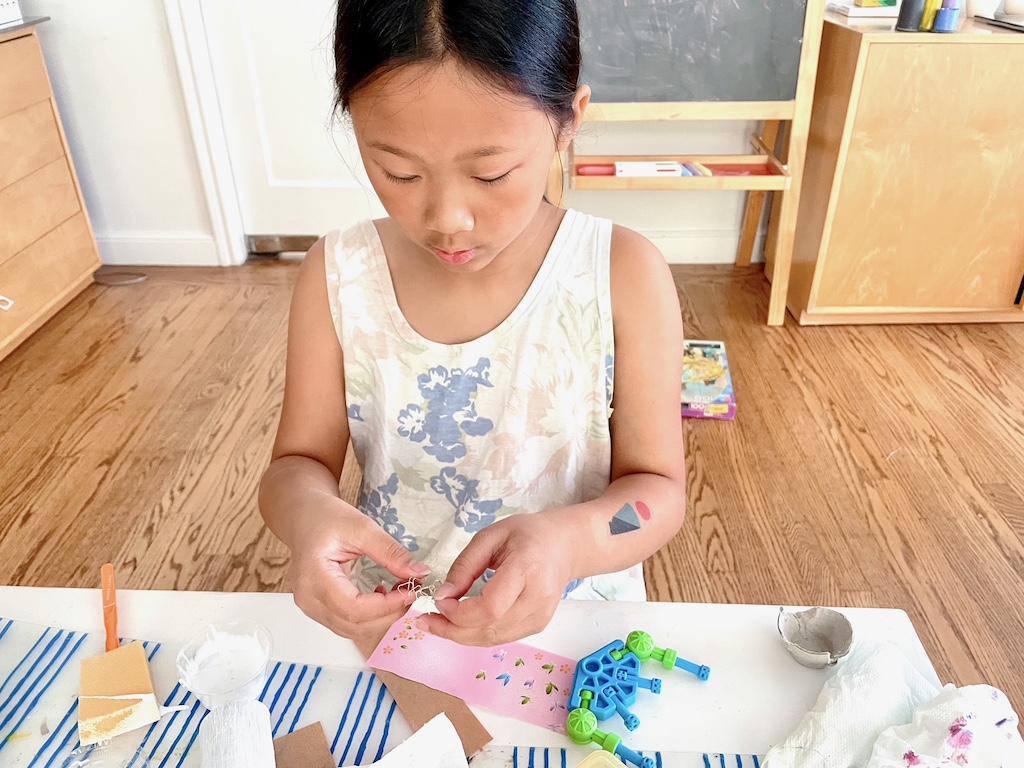 Child makes a puppet, entangling some wire for limbs.