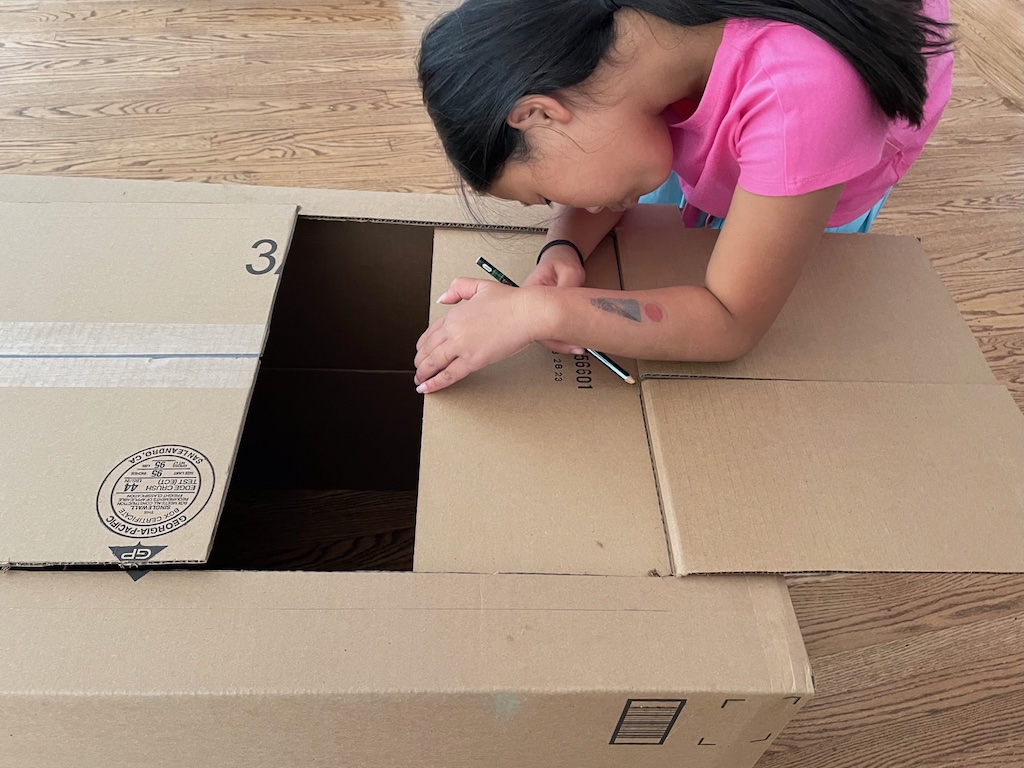 Child measures and cuts the carton for our puppet theater.