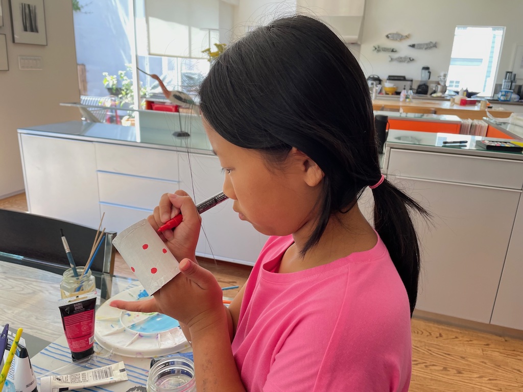Child decorates a white napkin ring with red dots.