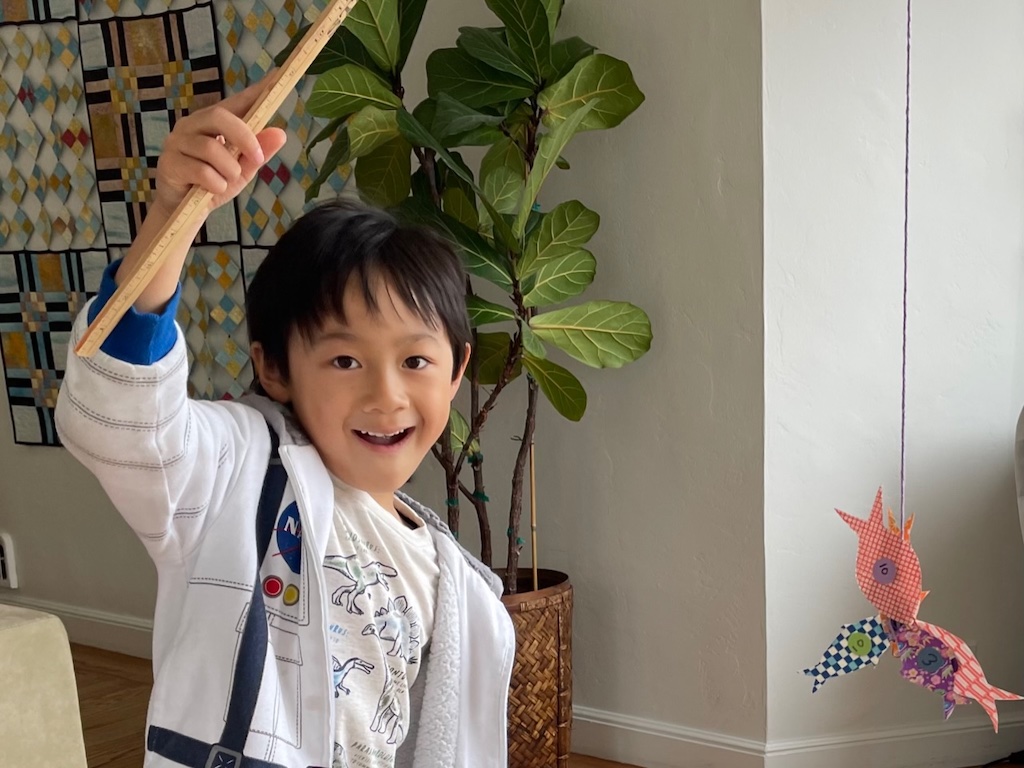 Cooling off with kids means indoor play during the heat of the day. Child plays a fishing game with paper fish hooked with a magnet pole.