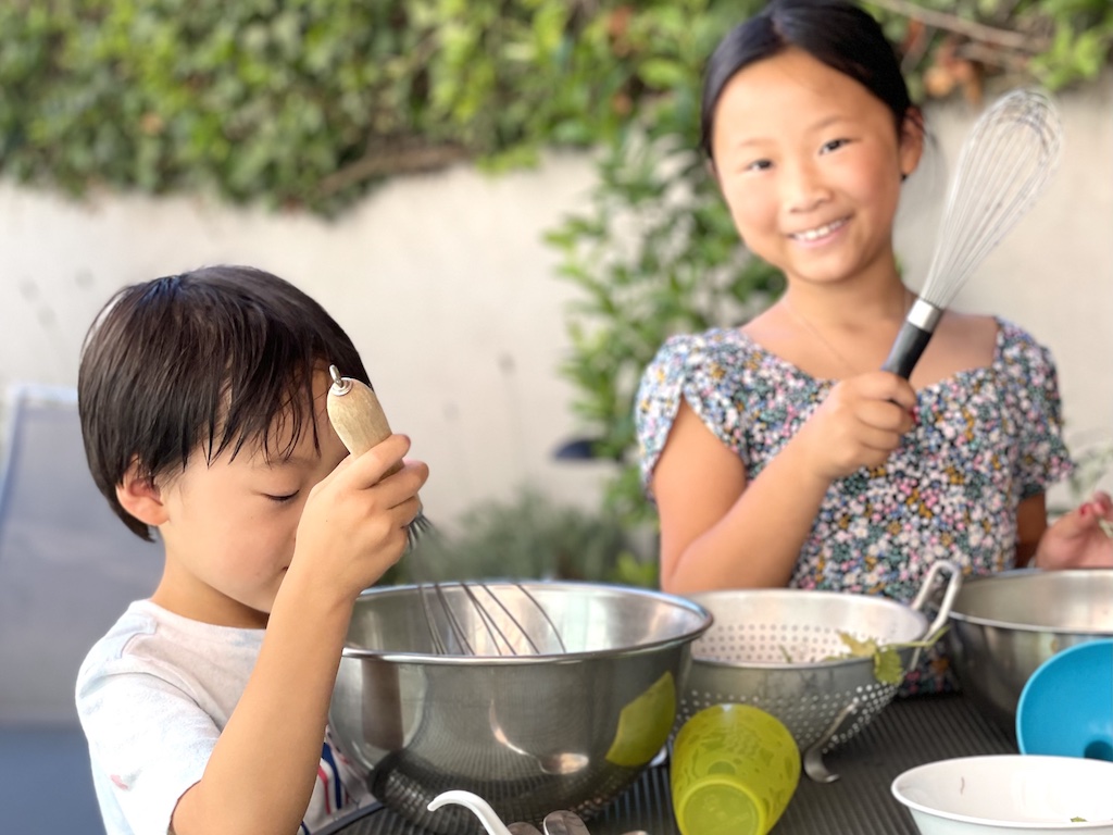 Kids pretending to cook with water outdoors, under an umbrella, when the day is coolest.
