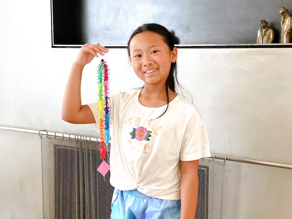 Child shows of her string of mini origami cranes. An origami sheet is glued to the bottom for the get well message.