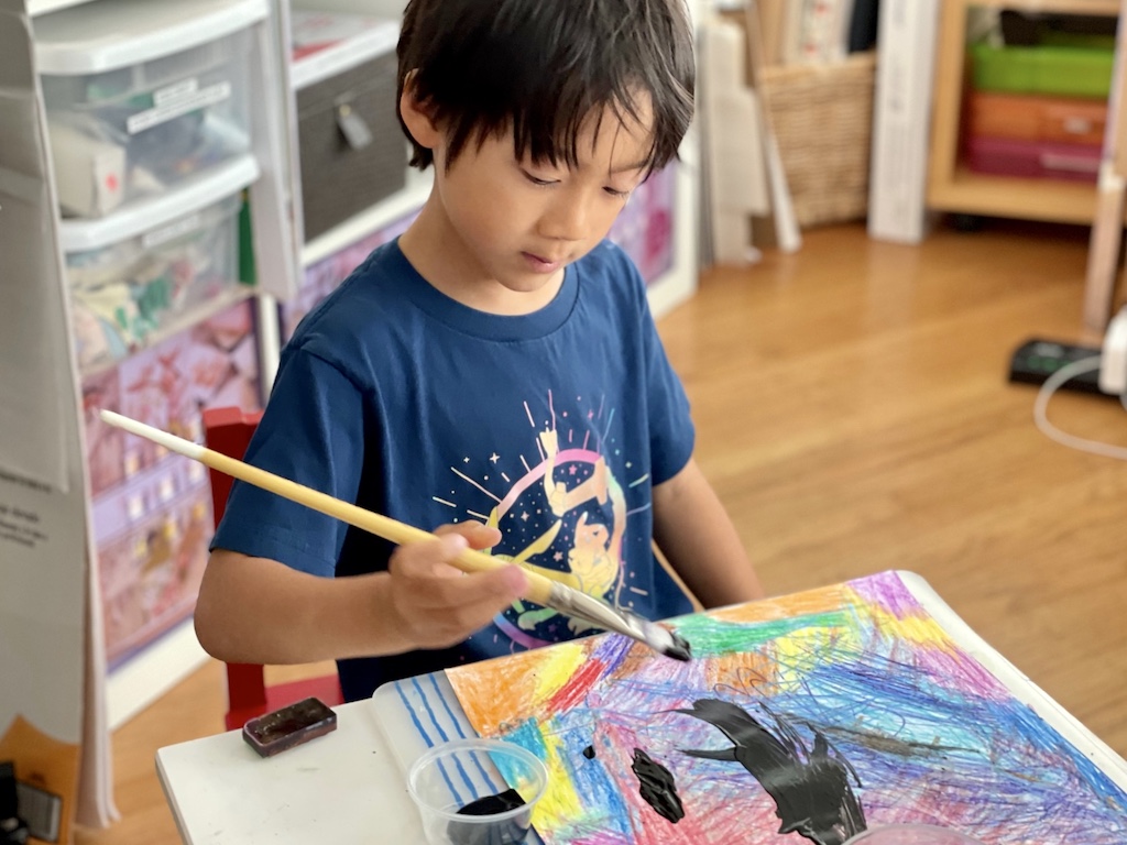 Child paints black poster paint over crayon to make crayon scratch art.