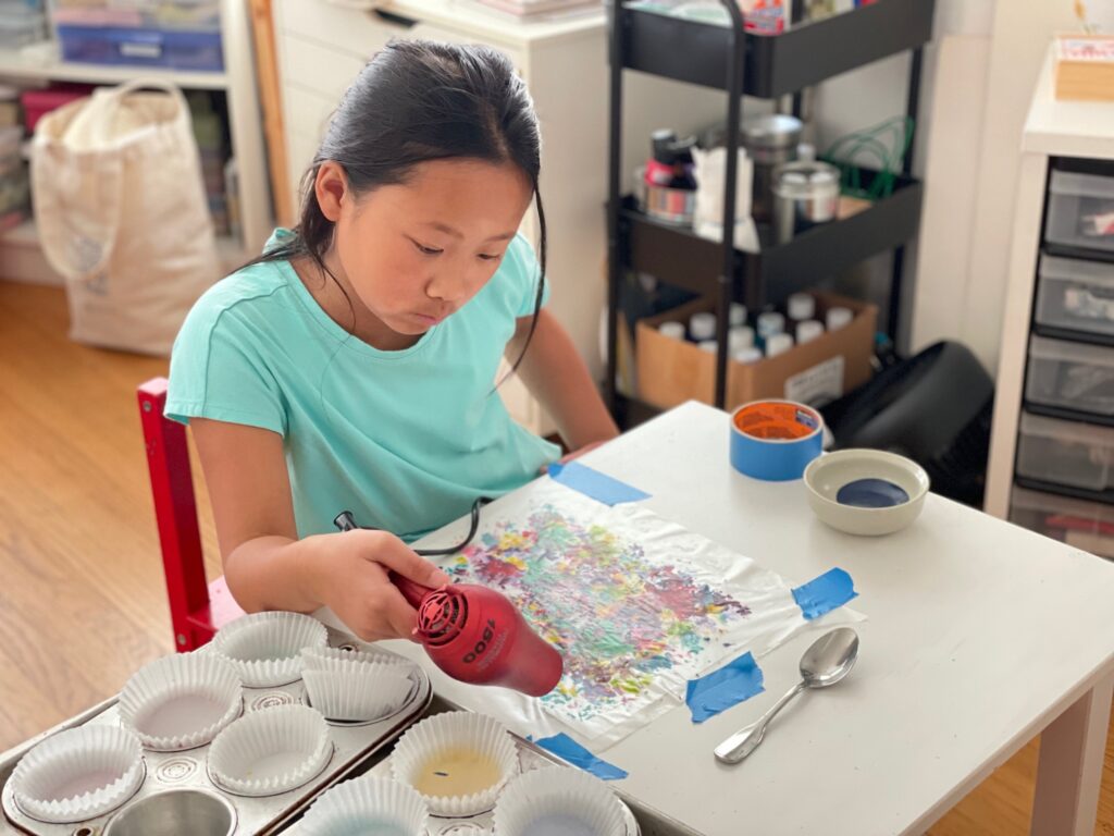 Child uses a hair dryer to melt crayons for her art project.