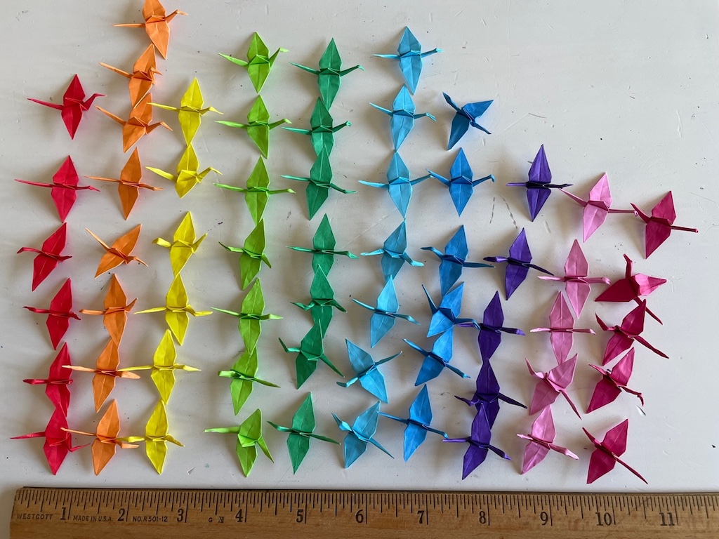 Some of the mini origami cranes made by Miss T in color order. Each folded crane is about 1 inch, from head to tail.