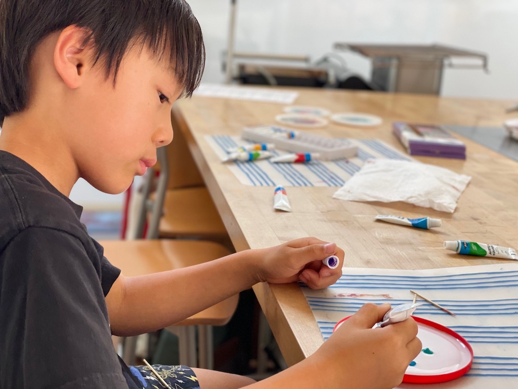 Child puts dots of paint on white school glue poured into a plastic lid.