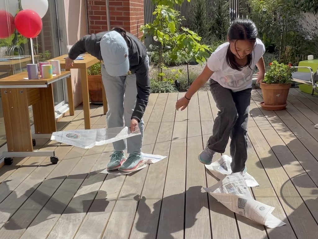 Mom and child in a relay race where you can only advance by stepping on newspapers.