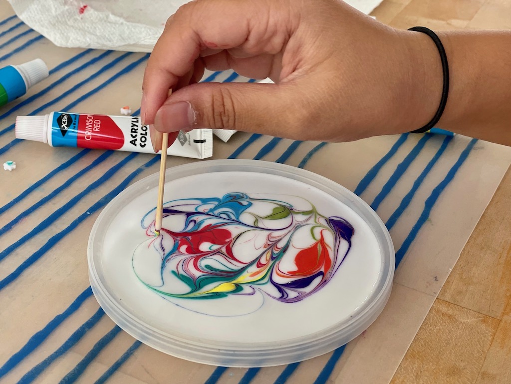 Child uses a toothpick to swirl the dots of glue to make a design.