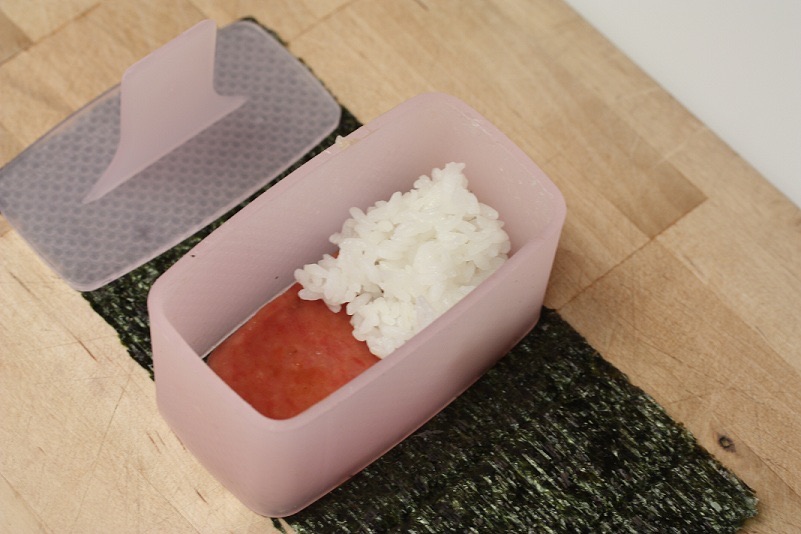 To make Spam musubi, lay nori on work surface, center the mold on top, then lay Spam and rice into the mold.