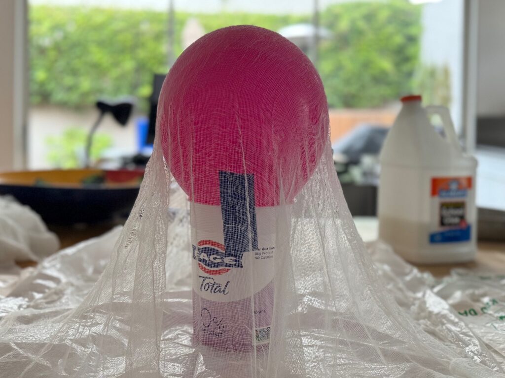 The balloon mold is covered with three layers of cheesecloth, each dipped in the glue/water mixture to solidify on the balloon and create the head.