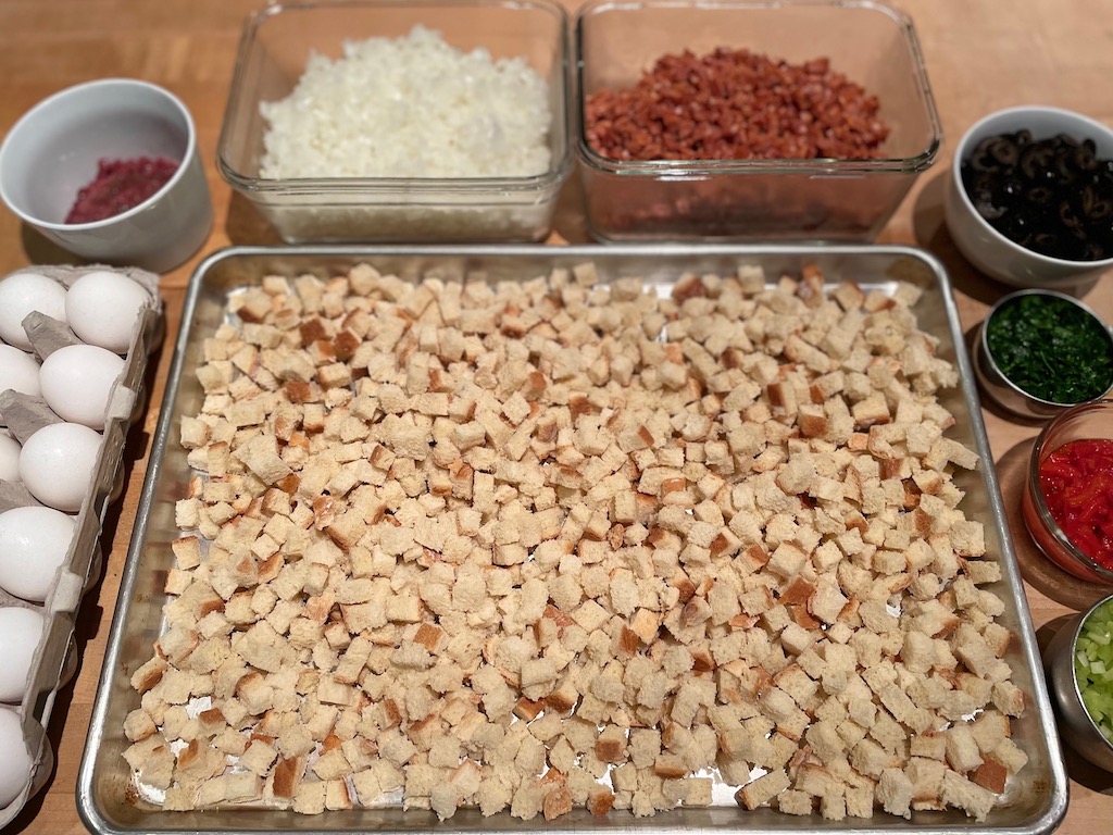 Ingredients for the Portuguese Thanksgiving Stuffing are laid out on the counter: eggs, giblets, onion, linguiça, olives, parsley, pimento, and celery.