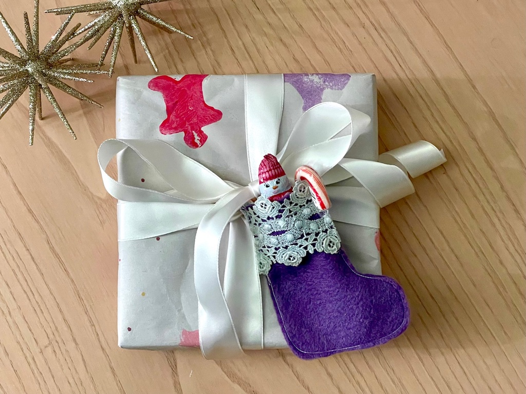 Tiny Christmas stocking is filled with candy and tied to a gift package for a tasty decoration.