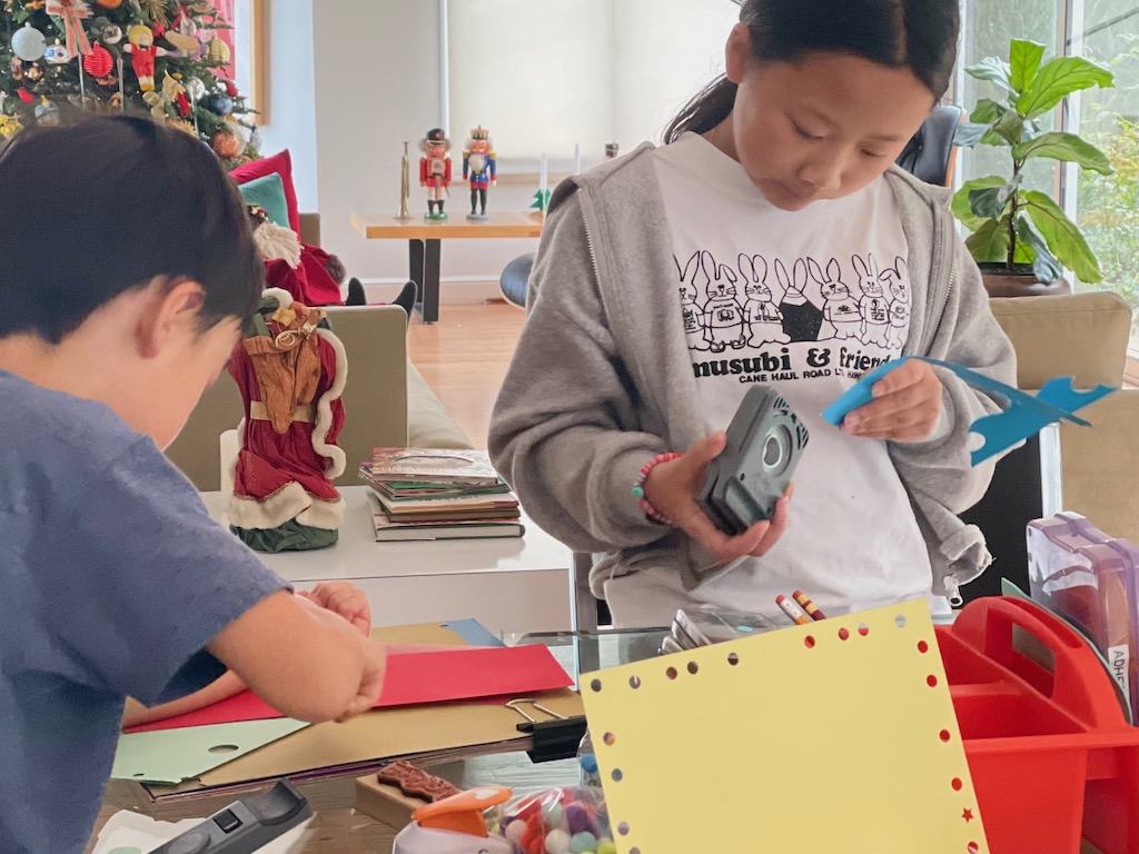 Kids making Christmas cards with paper punches and other tools.