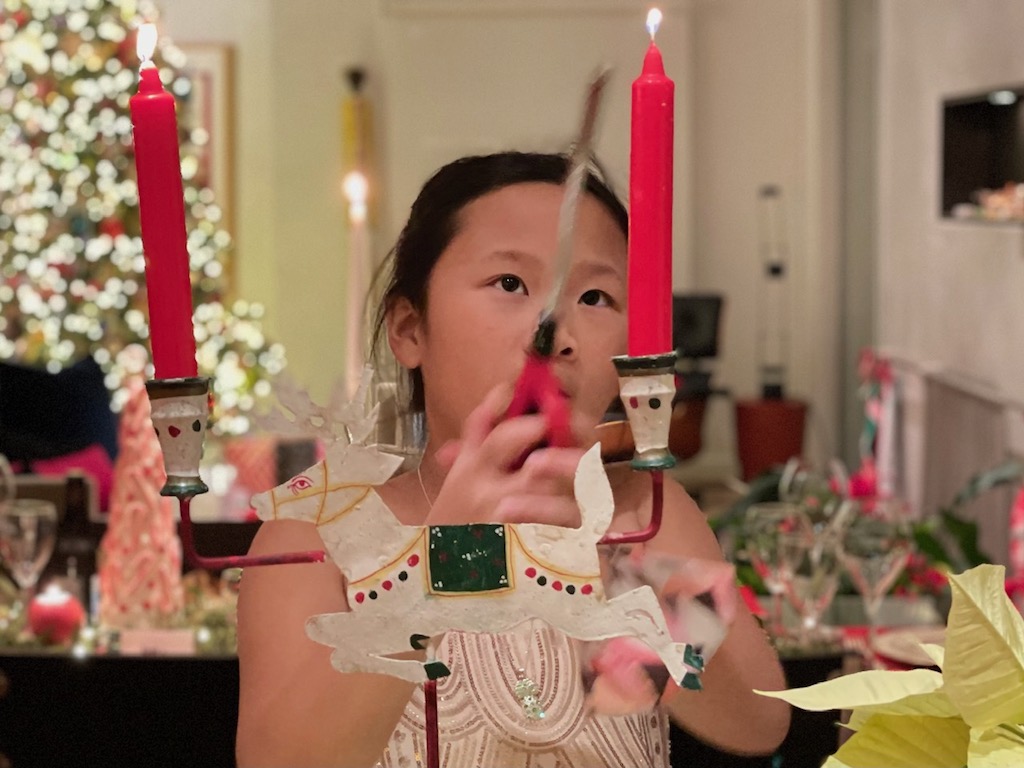 Children can help to prep for holiday events to pass on family traditions. A child lights the candles before Christmas Eve dinner.