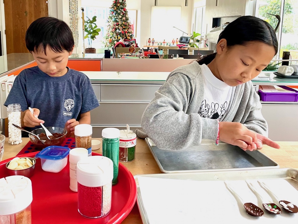 Kids make Hot Cocoa Stirring Spoons by dipping disposable spoons in chocolate and decorating with sprinkles.