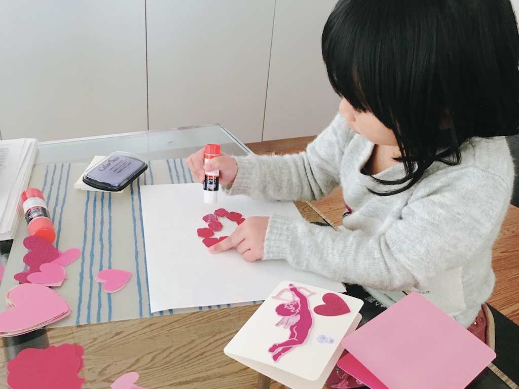 Young child gluing cutouts to make valentines.