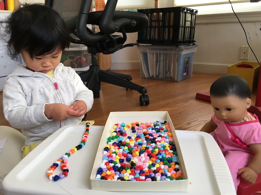 A smal child threads beads; a more complex project than making a lei.