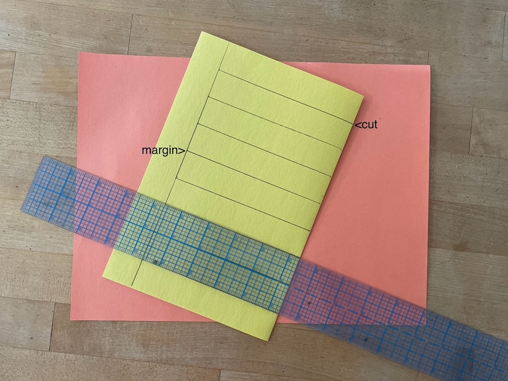 To make the backing for the placemat, fold construction paper in half crosswise, then rule a 1-inch margin at one edge, and perpendicular cutting lines across the paper.