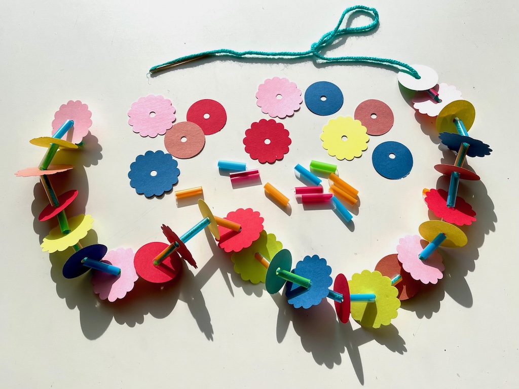 Elements of the paper lei: scallop-punched construction paper, circle-punched construction paper, straws, and yarn.