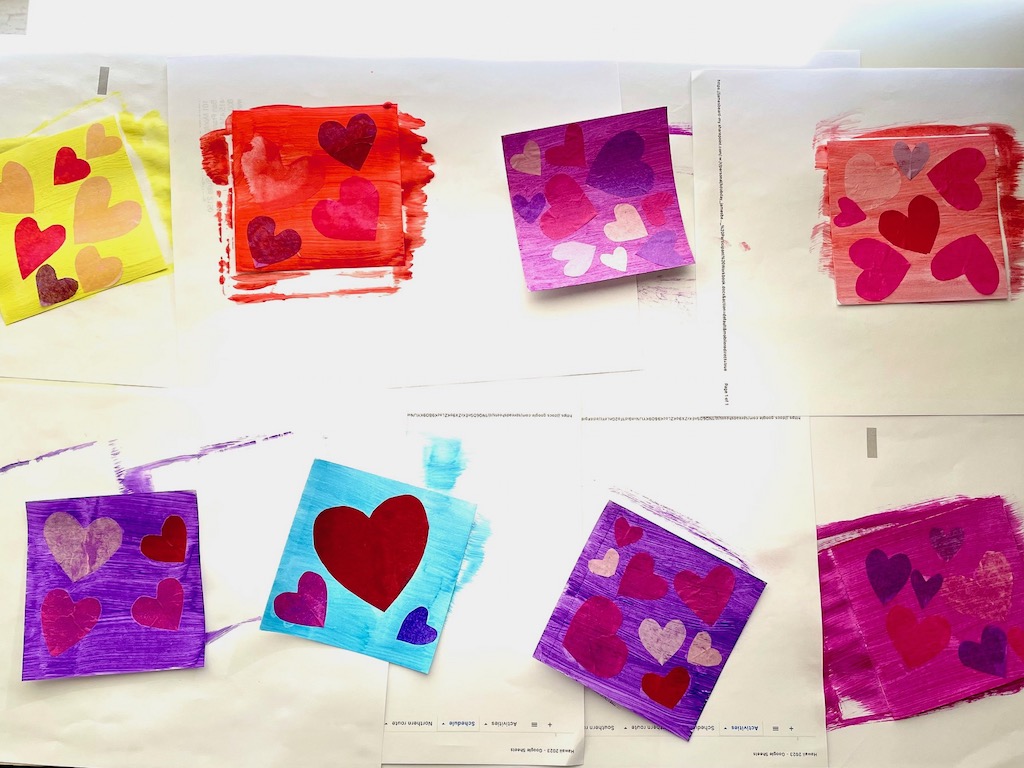 Painted squares with tissue paper hearts, in stages of drying.