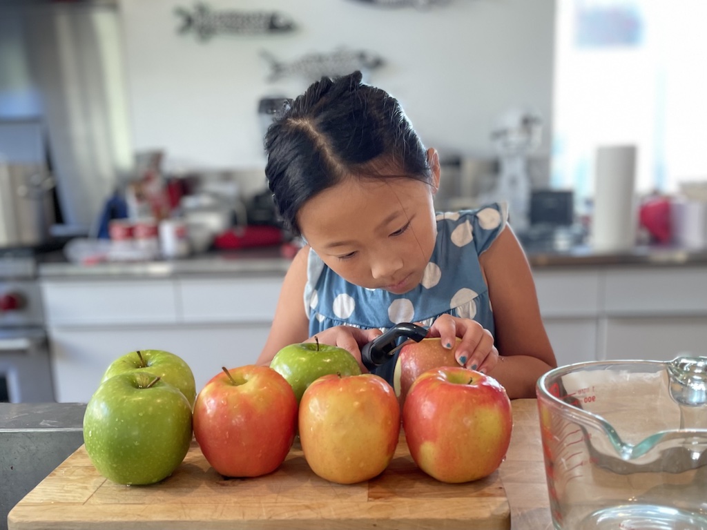 Older child peels apples for apple pie at Thanksgiving. Being comfortable in the kitchen from a young age builds confidence and competency.