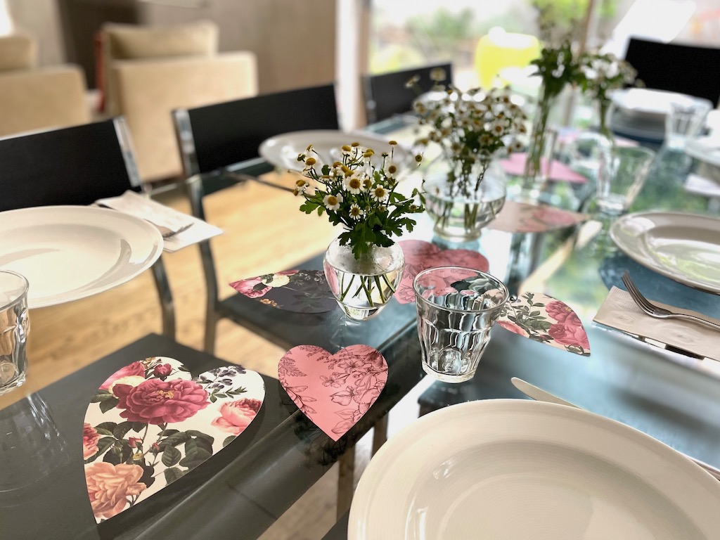 A simple Valentine table: white asters in mismatched vases with hearts cut from patterned cardstock scattered to make a runner.