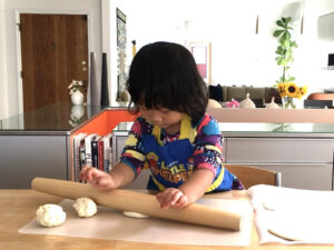 Preschooler rolling out pizza dough.