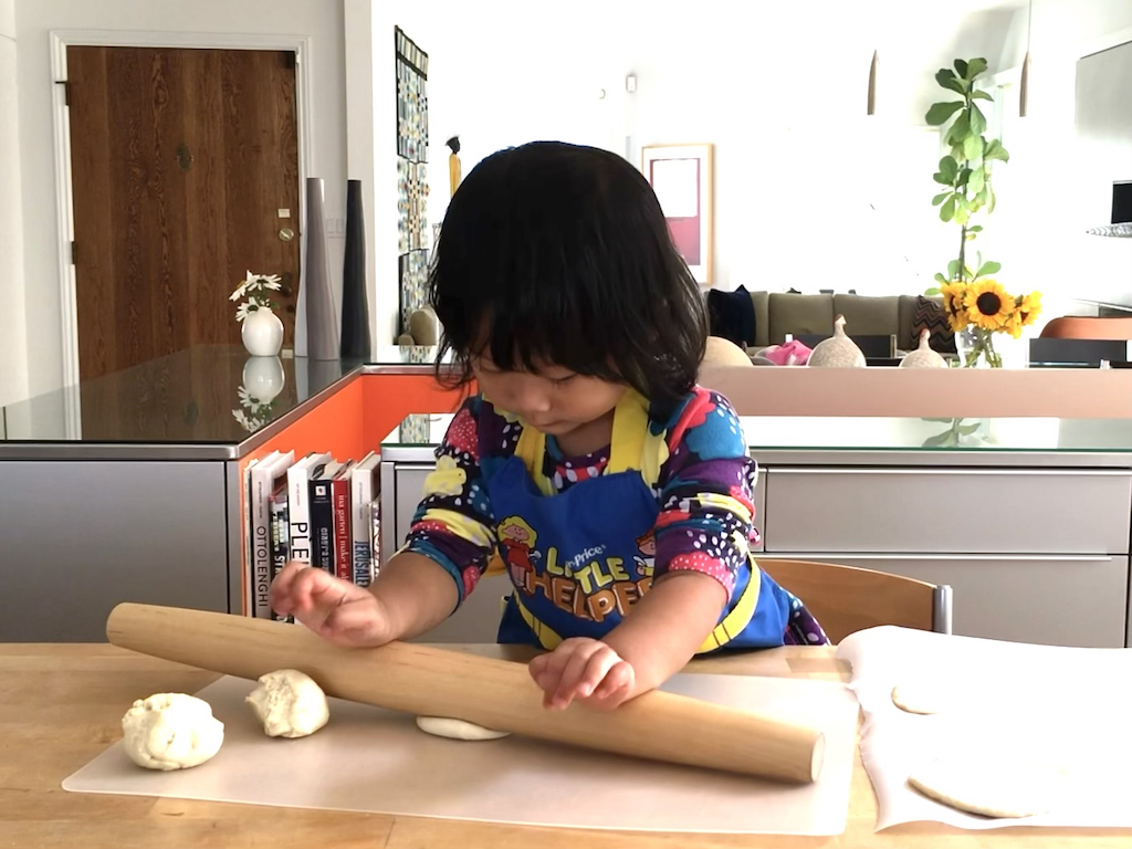Child nearly three years old, rolls out dough to make mini pizzas.
