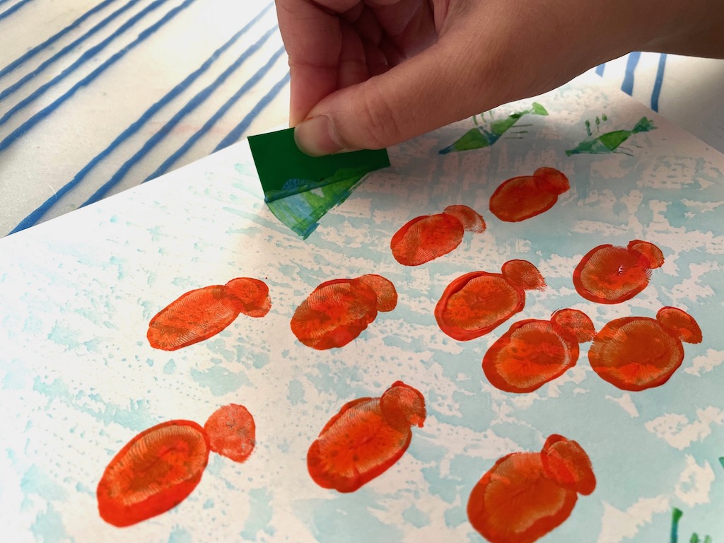 Child dips edge of cardboard in pain and then spreads paint in a fan shape to make the body.